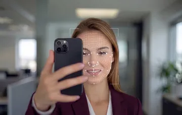 A woman taking a selfie while a facial-mapping mesh confirms she is physically present