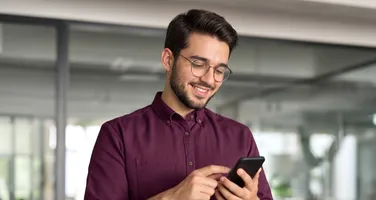 A man in glasses smiling at his phone in an office