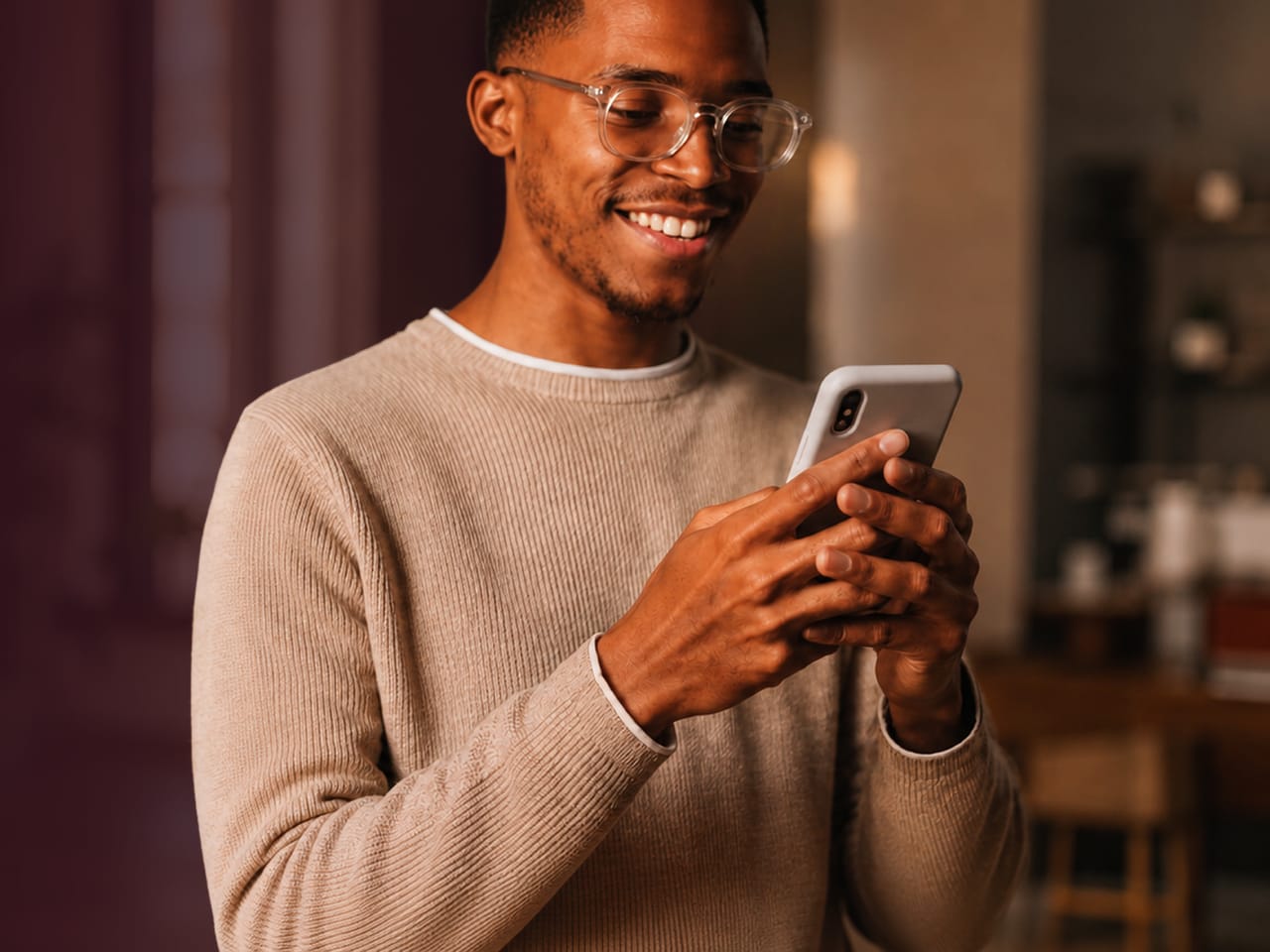 A man in clear-framed glasses smiling while using his phone